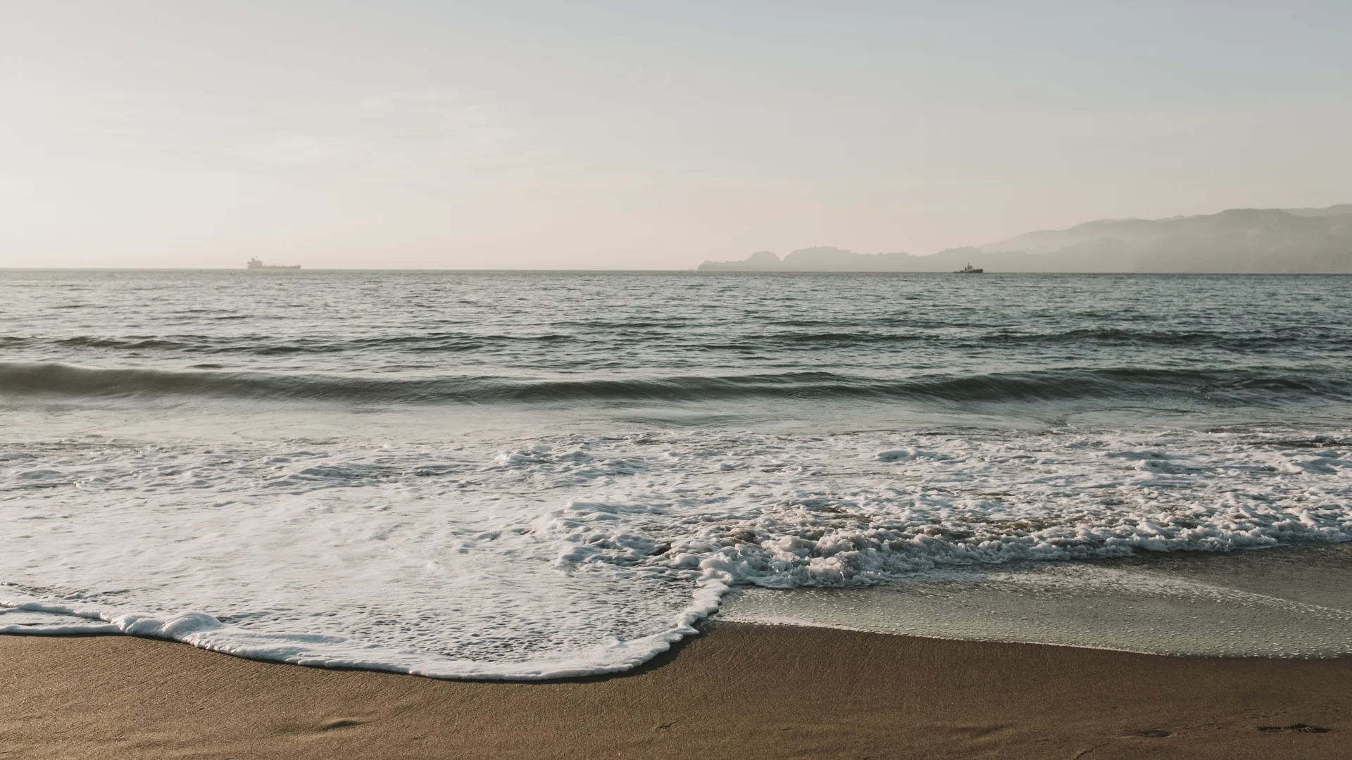 Waves rolling onto a quiet coast beneath a hazy horizon